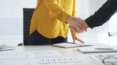 Profesyonel iş adamları el sıkışıyor, çağdaş ofis çalışma alanındaki toplantı masasının başında dururken ortaklık anlaşmasını onaylıyorlar. İş tokalaşması.