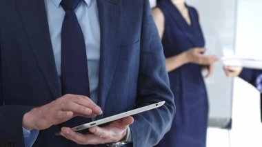 İş adamı şirket toplantısı sırasında dijital tablet hakkında bilgi kontrol ediyor, iş arkadaşlarıyla işbirliği yapıyor ve modern iletişim ve takım çalışması için teknoloji kullanıyor