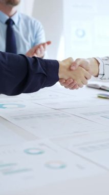 İş ortakları ofiste mali tablolar, dizüstü bilgisayarlar ve raporlarla el sıkışıyor, başarıyı simgeliyor, takım çalışması, anlaşma, işbirliği ve kurumsal büyümeyi simgeliyor