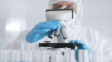 Koruyucu ekipman takan bilim araştırmacısı mikroskobu ayarlıyor, laboratuvar örneklerini steril araştırma ortamında hassasiyetle analiz ediyor. Tıp, sağlık ve bilim konsepti.