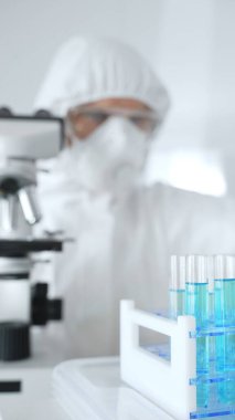 Koruyucu giysi giyen bilim araştırmacısı laboratuarda tıbbi araştırma deneyi yaparken deney tüplerine sıvıyı dikkatlice yerleştiriyor. Tıp, sağlık ve bilim konsepti.