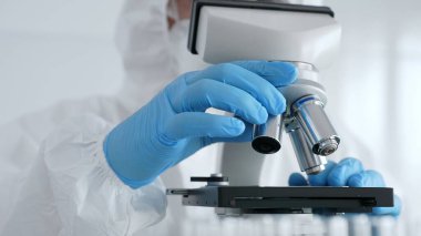 Laboratuvar araştırması sırasında mavi koruyucu eldiven takan bilim araştırmacısı ince ayar mikroskobu lensleri takıyor. Tıp, sağlık ve bilim konsepti.