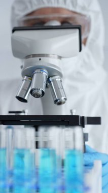 Mikroskop ayarlayan koruyucu ekipman takan bilimsel araştırmacı ya da virolog steril araştırma ortamında laboratuvar örneklerini hassasiyetle analiz ediyor. Tıp ve bilim konsepti.