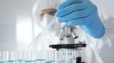 Koruyucu ekipman giyen bilimsel araştırmacıları kapatın, tıbbi araştırma yaparken dikkatlice test tüplerine sıvı pompalayın. Tıp ve bilim konsepti.