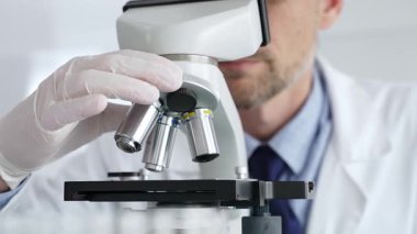 Beyaz koruyucu eldivenler giyen, laboratuvar mikroskobunu dikkatlice kalibre eden hassas tıbbi araştırma yapan erkek bilim araştırmacılarına yaklaş. Tıp ve bilim konsepti.