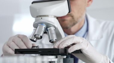 Beyaz koruyucu eldivenler giyen, laboratuvar mikroskobunu dikkatlice kalibre eden hassas tıbbi araştırma yapan erkek bilim araştırmacılarına yaklaş. Tıp ve bilim konsepti.