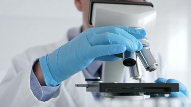 Beyaz önlüklü ve mavi eldivenli, mikroskop ayarlayan, modern laboratuarda ilaç araştırması yapan erkek bilim adamlarına yaklaş. Tıp ve bilim konsepti.