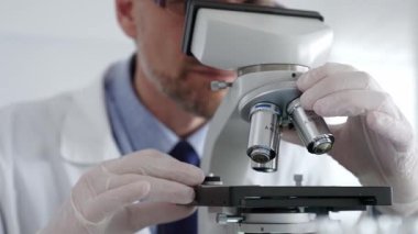 Beyaz koruyucu eldivenler giyen, laboratuvar mikroskobunu dikkatlice kalibre eden hassas tıbbi araştırma yapan erkek bilim araştırmacılarına yaklaş. Tıp ve bilim konsepti.