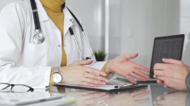 Doktor tıbbi bir randevu sırasında panoya notlar yazıyor, modern bir hastane ofisinde bir hastayla sağlık hakkında konuşuyor. Tıp, sağlık ve bilim konsepti