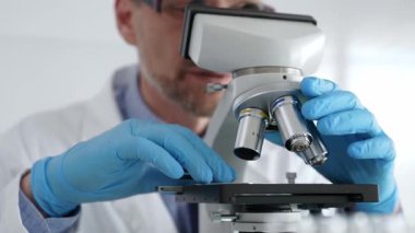 Beyaz önlüklü ve mavi eldivenli, mikroskop ayarlayan, modern laboratuarda ilaç araştırması yapan erkek bilim adamlarına yaklaş. Tıp ve bilim konsepti.