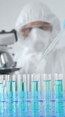 Koruyucu ekipman takan bilim araştırmacısı, tıbbi araştırma deneyi yaparken deney tüplerine sıvıyı dikkatlice yerleştiriyor. Tıp, sağlık ve bilim konsepti.