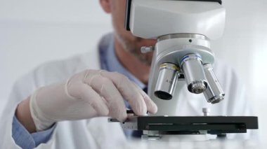 Beyaz koruyucu eldivenler giyen, laboratuvar mikroskobunu dikkatlice kalibre eden hassas tıbbi araştırma yapan erkek bilim araştırmacılarına yaklaş. Tıp ve bilim konsepti.