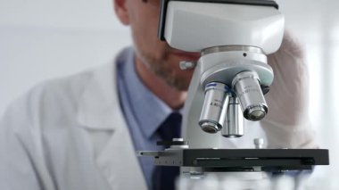Beyaz koruyucu eldivenler giyen, laboratuvar mikroskobunu dikkatlice kalibre eden hassas tıbbi araştırma yapan erkek bilim araştırmacılarına yaklaş. Tıp ve bilim konsepti.