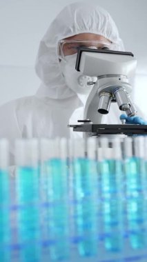 Koruyucu ekipman takan bilim araştırmacısı mikroskobu ayarlıyor, laboratuvar örneklerini steril araştırma ortamında hassasiyetle analiz ediyor. Tıp, sağlık ve bilim konsepti.