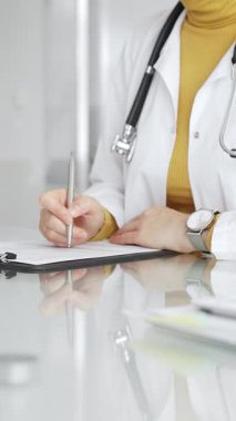 Tıbbi reçete yazan beyaz önlüklü ve steteskoplu bir doktor ya da klinikteki muayene sırasında hasta kayıtlarını dolduran. Tıp, sağlık ve bilim konsepti