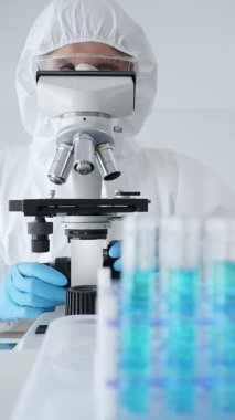 Koruyucu ekipman takan bilim araştırmacısı mikroskobu ayarlıyor, laboratuvar örneklerini steril araştırma ortamında hassasiyetle analiz ediyor. Tıp, sağlık ve bilim konsepti.
