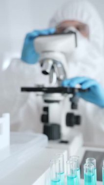 Laboratuvarda koruyucu dişli mikroskop lensleri takan bir bilimsel araştırmacının karşısında mavi sıvıyla test tüplerini kapatın. Tıp, sağlık ve bilim konsepti.