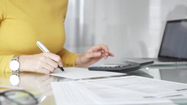 Kişisel mali işlerle ilgilenen, masrafları ve geliri hesaplayan, faturaları inceleyen ve masa başında vergi formları hazırlayan bir kadın. İş dünyasında denetim ve vergi teması