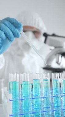 Koruyucu ekipman takan bilim araştırmacısı, tıbbi araştırma deneyi yaparken deney tüplerine sıvıyı dikkatlice yerleştiriyor. Tıp, sağlık ve bilim konsepti.