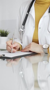 Tıbbi reçete yazan beyaz önlüklü ve steteskoplu bir doktor ya da klinikteki muayene sırasında hasta kayıtlarını dolduran. Tıp, sağlık ve bilim konsepti