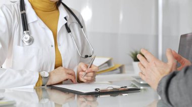 Doktor tıbbi bir randevu sırasında panoya notlar yazıyor, modern bir hastane ofisinde bir hastayla sağlık hakkında konuşuyor. Tıp, sağlık ve bilim konsepti