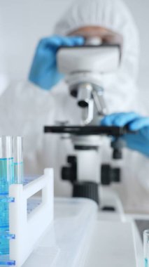 Laboratuvar araştırması sırasında mavi koruyucu eldiven takan bilim araştırmacısı ince ayar mikroskobu lensleri takıyor. Tıp, sağlık ve bilim konsepti.