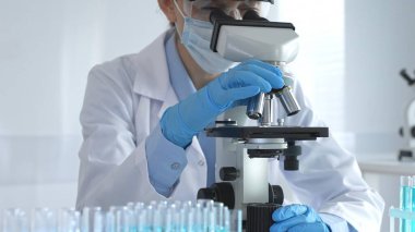 Koruyucu ekipman takan kadın bilim adamı mikroskop lenslerini dikkatlice ayarlıyor steril laboratuvar ortamında tıbbi araştırma örneklerini inceliyor.