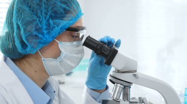 Koruyucu maske takan, gözlük takan ve mikroskop kullanarak laboratuvarda bilimsel araştırma yapan kadın bilim adamı. Tıp, sağlık ve bilim konsepti