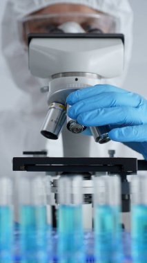 Mikroskop ayarlayan koruyucu ekipman takan bilimsel araştırmacı ya da virolog steril araştırma ortamında laboratuvar örneklerini hassasiyetle analiz ediyor. Tıp ve bilim konsepti.