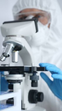 Mikroskop ayarlayan koruyucu ekipman takan bilimsel araştırmacı ya da virolog steril araştırma ortamında laboratuvar örneklerini hassasiyetle analiz ediyor. Tıp ve bilim konsepti.