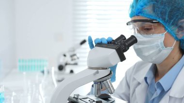 Koruyucu maske takan, gözlük takan ve mikroskop kullanarak laboratuvarda bilimsel araştırma yapan kadın bilim adamı. Tıp, sağlık ve bilim konsepti