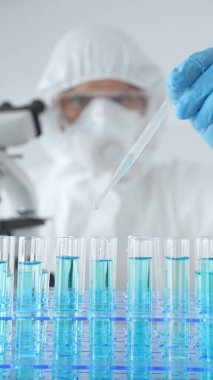 Koruyucu giysi giyen bilim araştırmacısı laboratuarda tıbbi araştırma deneyi yaparken deney tüplerine sıvıyı dikkatlice yerleştiriyor. Tıp, sağlık ve bilim konsepti.