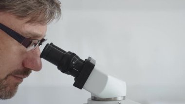 Bir erkek bilim adamının mikroskopla bakıp laboratuvar ortamında araştırma ve analiz yapması bilimsel araştırma ve keşifler sergilemesi. Tıp ve bilim konsepti.