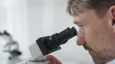 Yeni ilaçlar ve tedaviler geliştirmek için parlak ışıklı bir laboratuvarda mikroskopla gözlem yapan bir bilim adamına yakından bakın. Tıp ve bilim konsepti.