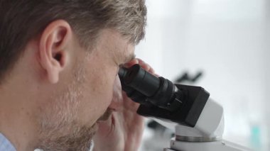 Yeni ilaçlar ve tedaviler geliştirmek için parlak ışıklı bir laboratuvarda mikroskopla gözlem yapan bir bilim adamına yakından bakın. Tıp ve bilim konsepti.