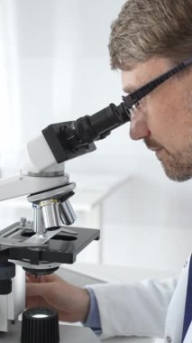 Gözlük takan erkek bilim adamı mikroskop altında araştırma ve analiz yaparak bilimsel araştırmaları ve keşifleri gösteriyor. Tıp ve bilim konsepti.