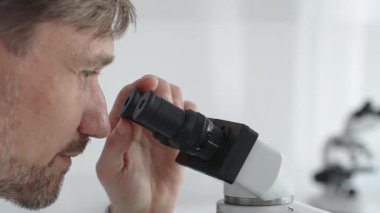 Yeni ilaçlar ve tedaviler geliştirmek için parlak ışıklı bir laboratuvarda mikroskopla gözlem yapan bir bilim adamına yakından bakın. Tıp ve bilim konsepti.