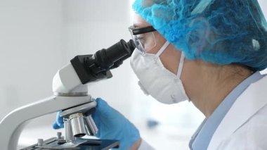Bir laboratuarda mikroskop kullanarak maske ve gözlük takan kadın bir bilim adamı araştırma ve bilimsel keşifte bulundu. Laboratuvar ve bilim konsepti.