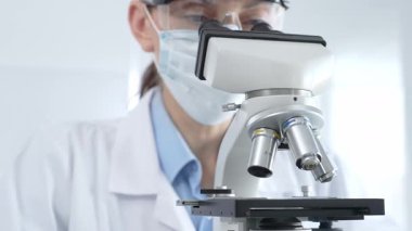 Dişi bilim araştırmacısı mikroskop lenslerini dikkatlice ayarlayıp steril laboratuvar ortamındaki hassas işlere odaklanıyor. Tıp, sağlık ve bilim konsepti.