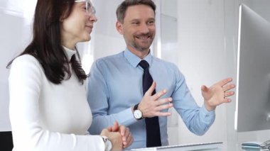 İş arkadaşları ofis masasında iş birliği yapıyor, projeyi bilgisayarda tartışıyor, erkek şirket toplantısı sırasında ekran içeriğini anlatıyor, tavsiye veriyor ve destek veriyor.