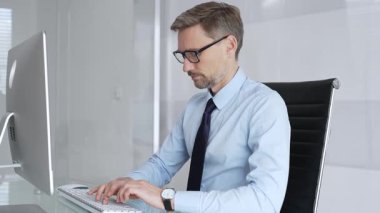 İşadamı dikkatle bir bilgisayar ekranına odaklanıyor, bir ofis masasında oturuyor ve bir klavyeye yazı yazıyor, çalışmaya ve dijital iletişime olan bağlılığını temsil ediyor