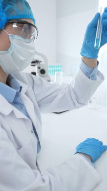 Mavi kapaklı, eldivenli ve Google 'lı tıp bilimi araştırmacısı laboratuvar çalışma alanında test tüpündeki sıvıyı inceliyor. İlaç ve sağlık hizmetleri kavramı.
