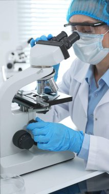 Kadın bilim adamı mikroskop ile numune analiz ediyor, tıbbi araştırma sırasında koruyucu laboratuvar giysileri giyiyor. Tıp, laboratuvar ve bilim konsepti.