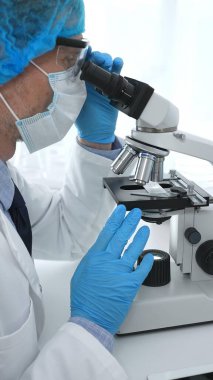 Koruyucu maske takan kıdemli erkek bilim adamı laboratuarda mikroskop kullanarak tıbbi araştırma ve analiz yapıyor. Tıp, sağlık ve bilim konsepti.