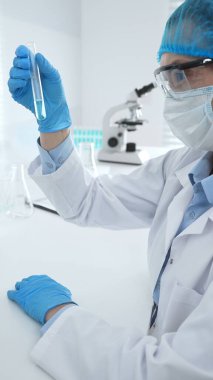 Mavi kapaklı, eldivenli ve Google 'lı tıp bilimi araştırmacısı laboratuvar çalışma alanında test tüpündeki sıvıyı inceliyor. İlaç ve sağlık hizmetleri kavramı.