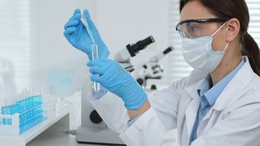 Laboratuvar analizi sırasında cam şişeye kimyasal solüsyon yerleştiren koruyucu giysi araştırmacısı, beyaz arka plan. Tıp, sağlık ve bilim konsepti