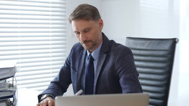 Profesyonel iş adamı dizüstü bilgisayarla uğraşırken yakın çevresindeki organize klasörlerle şık çalışma sahalarında konumlanıyor ve kurumsal ithafı vurguluyor. İş dünyasında denetim ve vergi teması