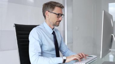 İşadamı dikkatle bir bilgisayar ekranına odaklanıyor, bir ofis masasında oturuyor ve bir klavyeye yazı yazıyor, çalışmaya ve dijital iletişime olan bağlılığını temsil ediyor