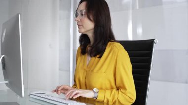 Ofis masasındaki dizüstü bilgisayara odaklanmış sarı günlük bluz ve gözlük giyen profesyonel bir kadın iş görevleri için veri yazıp analiz ediyor. İş dünyasında denetim.