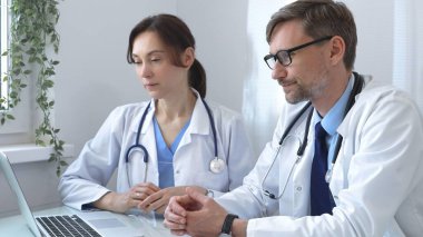 İki doktor bir dizüstü bilgisayardaki tıbbi kayıtları inceliyor, bir hastane veya klinik ortamdaki hasta verileri üzerine odaklanmış bir tartışmaya giriyorlar. İlaç ve sağlık hizmetleri kavramı.